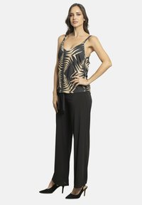 Pantalones negros de pierna ancha combinados con una blusa sin mangas que presenta un patrón abstracto en beige y negro. Tejido suave y corte a medida.