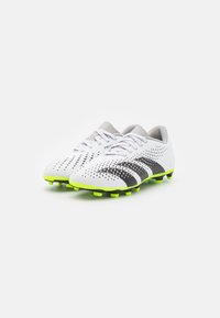 Botas de fútbol blancas con rayas negras, diseño perforado y suelas de color verde brillante. El material es sintético con una textura suave y cordones.
