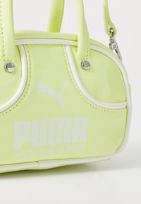 Gul lackläderväska med vita detaljer, rundad form, dubbla handtag upptill och en framträdande Puma-logotyp i vit text.