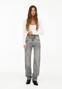 Fitted white long-sleeve top, high-waisted gray denim wide-leg jeans with slight fading and visible stitching, complemented by black ankle boots.