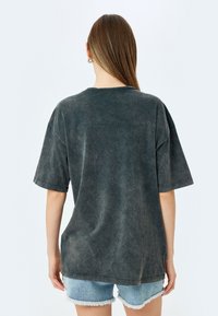 Mørkegrå oversized T-shirt med korte ærmer, rundet halsudskæring og en let falmet tekstur, parret med lyse denimshorts.