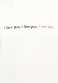 Άσπρο πουκάμισο με τη φράση «Σε αγαπώ.» επαναλαμβανόμενη τρεις φορές σε γραφικό χαρακτήρα, με την τελευταία επανάληψη σε πορτοκαλί κείμενο.