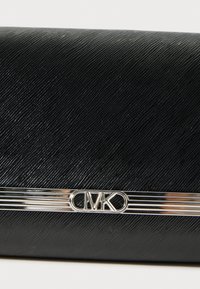 Clutch nera texturizzata in PVC con un accento in logo CMK argentato e strisce metalliche orizzontali nella parte inferiore. Finitura della superficie liscia.