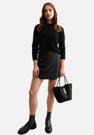 Maglione nero, gonna grigia a righe, borsa nera con un accentuazione dorata e scarpe nere con calzini. L'outfit presenta un design sartoriale.