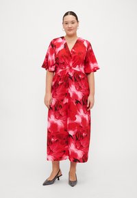 Vestido floral vermelho com mangas curtas, decote em V e cintura ajustada. Apresenta uma mistura de tons claros e escuros, com um design fluido e pernas largas.