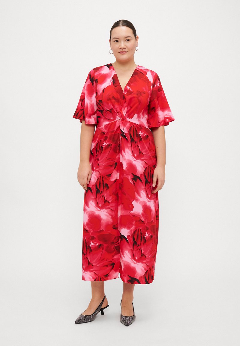Vestido floral vermelho com mangas curtas, decote em V e cintura ajustada. Apresenta uma mistura de tons claros e escuros, com um design fluido e pernas largas.