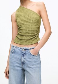 Haut asymétrique vert olive avec tissu texturé et froncé. Associé à un jean taille haute bleu clair déchiré avec bords effilochés.