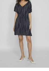 Mekko tummansinisestä kankaasta, jossa on valkoisia pystysuoria raitoja, V-mallinen kaula-aukko ja väljä leikkaus. Yhdistetty valkoisiin kärkitossuihin, sileä rakenne.