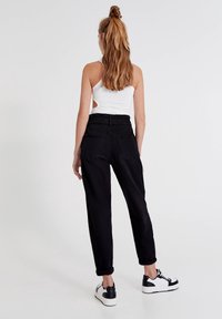 Svarta byxor med lös passform, elastisk midja och två bakfickor, ihopparat med en vit linne och svarta och vita sneakers.