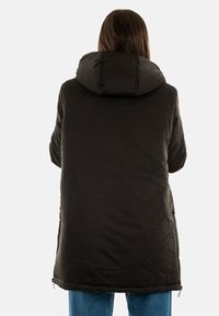Abrigo negro tipo puffa con capucha, corte a media longitud, bolsillos laterales con cremallera y tejido texturizado con costuras visibles.