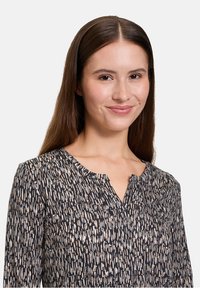 Schwarze Bluse mit einem geometrischen Muster in Beige und Creme. Verfügt über einen runden Halsausschnitt, lange Ärmel und einen strukturierten Stoff.