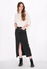Maglione bianco a maglia con trama aperta e gonna di jeans nera con spacco anteriore. Gli stivali neri con lacci completano l'outfit.