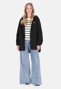 Fekete, túlméretezett kapucnis kabát, fehér és tengerészkék csíkos ing fölött viselve, bőszárú kék farmerrel és fehér tornacipővel párosítva.