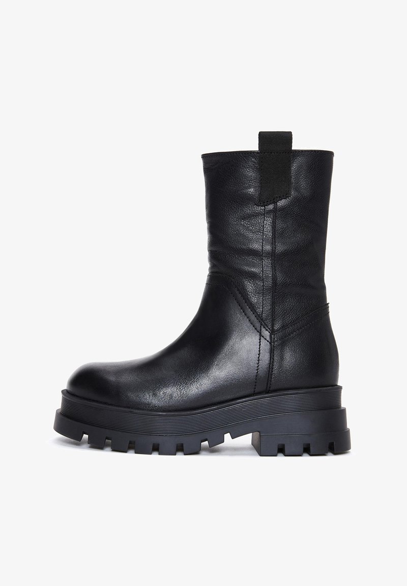 Botín de cuero negro con forma afilada, suela gruesa de goma y una lengüeta en la parte trasera. Presenta detalles cosidos y una textura suave.