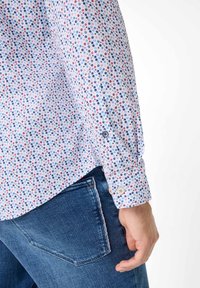 Hvid langærmet skjorte med et flerfarvet prikmønster. Har knapmanchetter og en lige kant, og bæres sammen med mørke denimjeans.