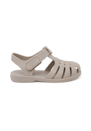Sandale pour enfants couleur beige clair, fabriquée en plastique flexible. Présente un design à bout ouvert, une sangle réglable et une semelle intérieure texturée surélevée pour une meilleure adhérence.