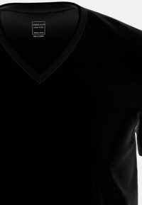 T-shirt nera a collo a V realizzata in cotone biologico, con maniche corte e una superficie liscia. L'etichetta riporta "Ammann - Made in Europe."