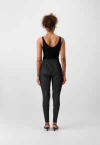 Bodysuit noir à côtes associé à un pantalon noir ajusté taille haute. Texture lisse et silhouette épurée. Sandales à talons noires à lanières complètent le look.