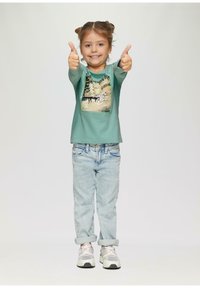 Chemise à manches longues vert menthe avec impression graphique, associée à un jean bleu clair retroussé et des baskets grises avec des accents blancs.