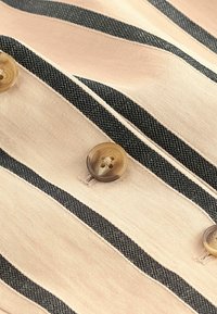 Tissu rayé en rose pâle avec des lignes noires, présentant de grands boutons ronds marron. La texture semble lisse avec un léger éclat.
