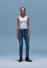 Witte tanktop, blauwe jeans en zwarte enkellaarsjes. De outfit heeft een eenvoudig ontwerp, met een getailleerde snit en lichte denim.
