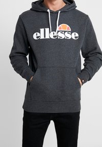Felpa con cappuccio di colore grigio scuro, dotata di una tasca frontale, stringhe bianche e un grande logo "ellesse" bianco con un accento arancione e giallo sopra.