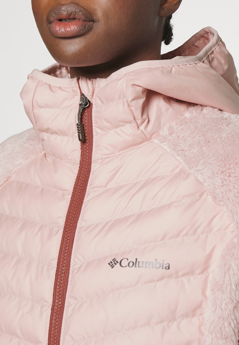 Rosa Columbia Jacke mit einem gesteppten Design, das auf einer Seite eine weiche, fellähnliche Textur hat, sowie einem Reißverschluss mit einem bordeauxfarbenen Akzent.