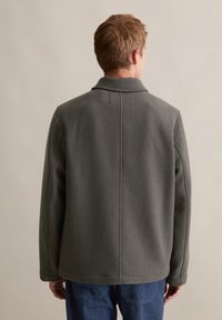 Grijze wollen blend-jack met een gestructureerde kraag, zichtbare naden en een ontspannen pasvorm, gecombineerd met blauwe denim broeken.