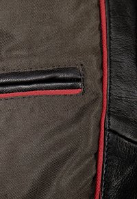 Zwarte leren accenten op olijfgroen stof met een opvallende rode stiksel langs de rand en een klein patch zakje.