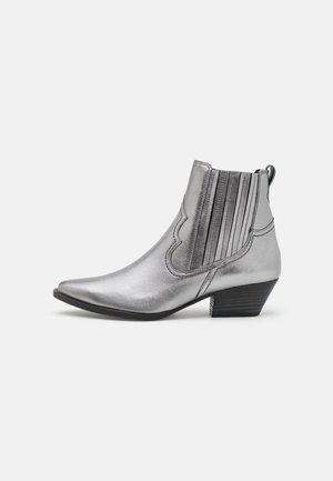 Botines metálicos plateados con puntera puntiaguda, detalles ondulados y paneles elásticos con rayas verticales. Tacón bajo tipo bloque. Textura suave.