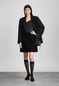 Μαύρο σακάκι πάνω από γκρι τοπ, συνδυασμένο με μαύρη φούστα. Το μοντέλο φοράει διαφανείς μαύρες κάλτσες μέχρι το γόνατο και μαύρα σε μπούλινγκ παπούτσια, κρατώντας μια τσάντα με χάντρες.