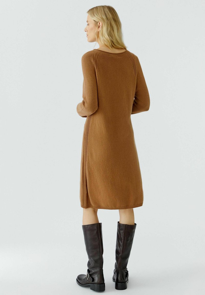 Braunes gestricktes Kleid mit rundem Ausschnitt und langen Ärmeln, das seitliche gerippte Akzente aufweist. Matt schwarze knielange Stiefel runden den Look ab.