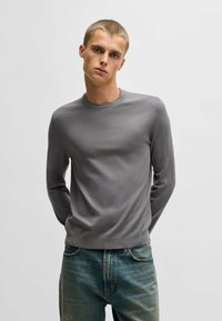 Graues Langarmshirt mit Rundhalsausschnitt, taillierter Passform und glatter Textur, kombiniert mit verwaschenen blauen Jeans.