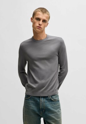 Gray long-sleeve shirt with a round neckline, fitted design, and smooth texture, paired with faded blue jeans.