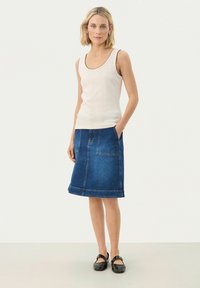 White patterned tank top with black trim, paired with a knee-length dark denim skirt featuring two front pockets and a hemmed edge. Black shoes.
