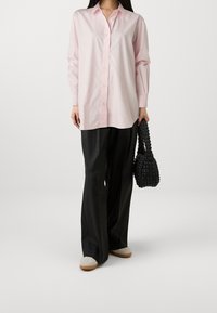 Light pink button-down shirt with long sleeves, paired with black wide-leg trousers and a textured black woven handbag.