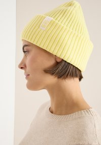 Bonnet en maille côtelée jaune avec revers, orné d'une étiquette logo décontractée sur le côté. Texture douce, forme conique et ajustement confortable.