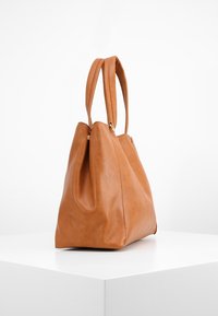 Kodin nahkainen kassi, jossa on jämäkkä muoto, kaksi kahvaa ja pehmeä pinta. Ominaisuuksiin kuuluu pleatattu muotoilu ja vähäiset metalliosat.