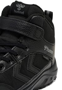 Nærbillede af sort Hummel højtop sneaker med læderrem, stofpaneler, reflekterende logo og tekstureret gummisål.