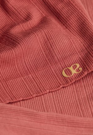 Geribbelde stoffen top in een gedempte rozenkleur met een zachte textuur; voorzien van een opvallend goudkleurig logo-accent. Gedetailleerde close-upweergave.