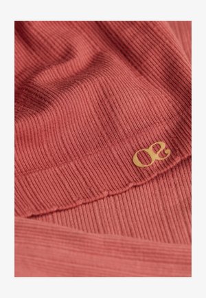 Geribbelde stoffen top in een gedempte rozenkleur met een zachte textuur; voorzien van een opvallend goudkleurig logo-accent. Gedetailleerde close-upweergave.