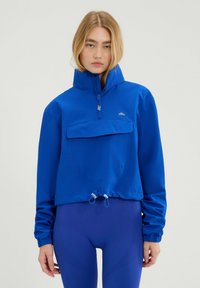 Blauwe cropped jasje gemaakt van lichtgewicht materiaal, met een hoge kraag, een voorzak en een verstelbare trekkoord aan de onderkant.