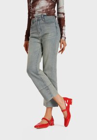 Jeans in denim chiaro con vestibilità dritta, abbinati a eleganti ballerine in pelle verniciata rossa con cinturino alla caviglia.