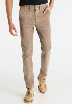Tan corduroy pants with a slim fit, featuring a button closure, five pockets, and a soft, textured surface. Paired with beige lace-up boots.