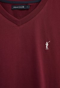 Polo Club col en V bordeaux avec petit logo joueur de polo brodé en blanc sur la poitrine gauche et étiquette noire taille M sur le col.