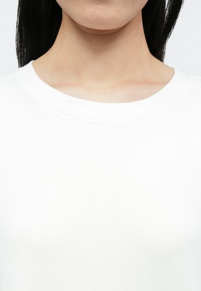 Biały bawełniany top z okrągłym dekoltem o gładkiej fakturze i klasycznym kroju, z prostym wycięciem przy szyi, bez widocznych wzorów ani zdobień.