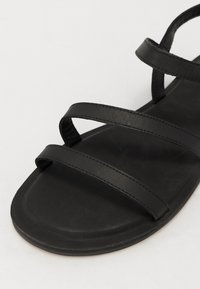 Sandalia plana negra con tres tiras de cuero estrechas. Textura suave y plantilla contorneada, con un diseño minimalista y sin acentos adicionales.