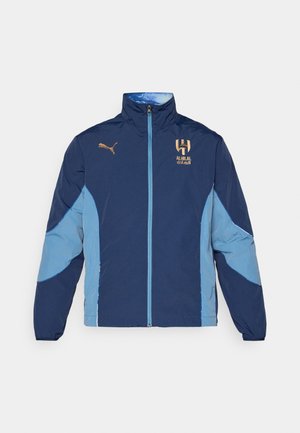 Marineblaue und hellblaue Polyesterjacke mit Reißverschluss, Stehkragen, Logo-Akzenten und einem farblich abgesetzten Design an den Ärmeln.