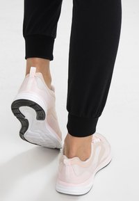 Helle rosa Sporttaschen mit Obermaterial aus Mesh, Gummisohle und gepolstertem Kragen, kombiniert mit schwarzen Jogginghosen und einem minimalistischen Design.