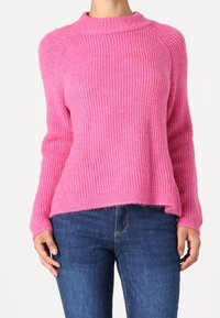 Pull rose tricoté avec un col haut, une texture côtelée et une coupe légèrement ample, assorti à un jean en denim bleu.